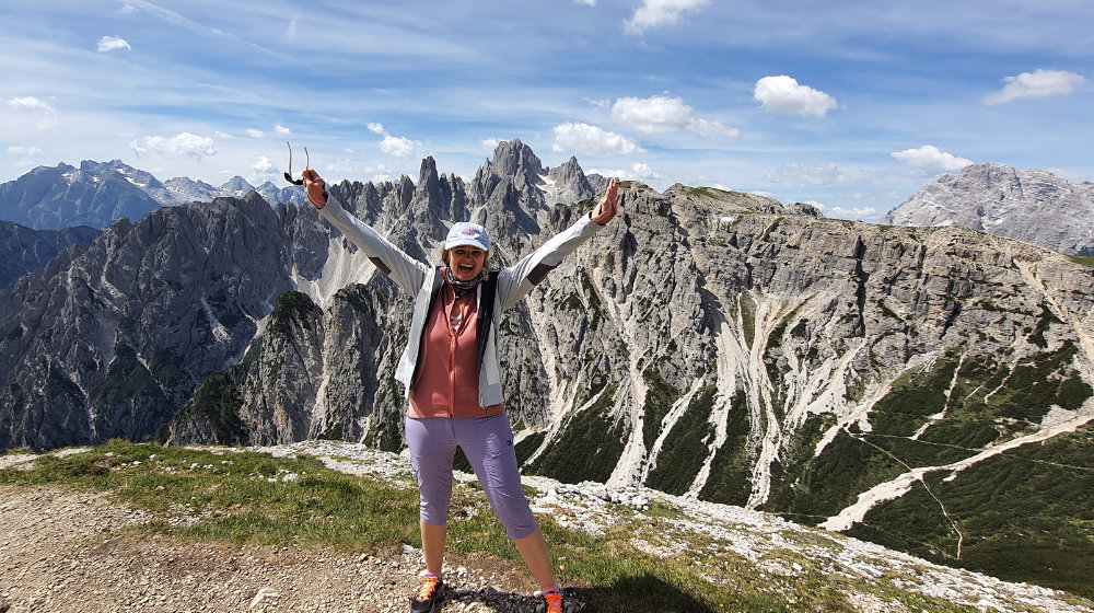 Susa reißt Arme begeistert nach oben, im Hintergrund Gipfel der Dolomiten