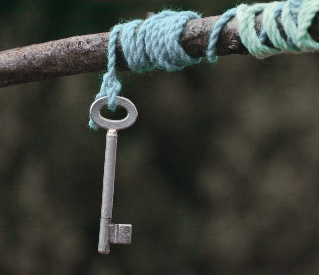 Schlüssel zum Sprechen, silberner Schlüssel hängt an hellblauem faden, der um einen Zweig gewickelt ist